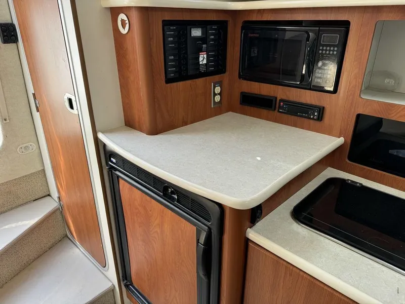Slide: The Image of 2005 Bayliner 305 boat interior kitchen with microwave, fridge, and wooden cabinetry. - 10