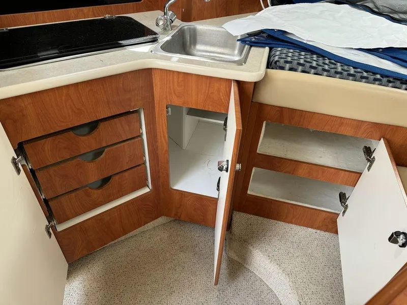 Slide: The Image of 2005 Bayliner 305 interior kitchen with open cabinets and sink, showcasing wood finish and storage. - 12