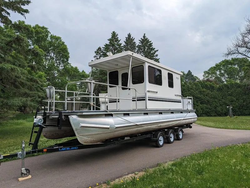 Slide: The Image of Custom 2010 River Time Houseboat on trailer, surrounded by lush greenery and trees. - 12
