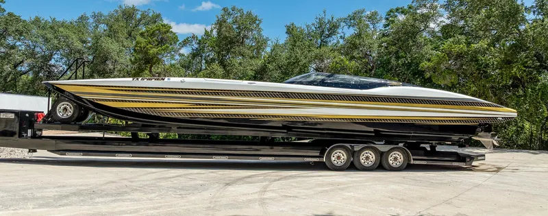 Slide: The Image of 2017 MTI 48 speedboat on trailer, featuring sleek design and gold accents, surrounded by trees. - 12