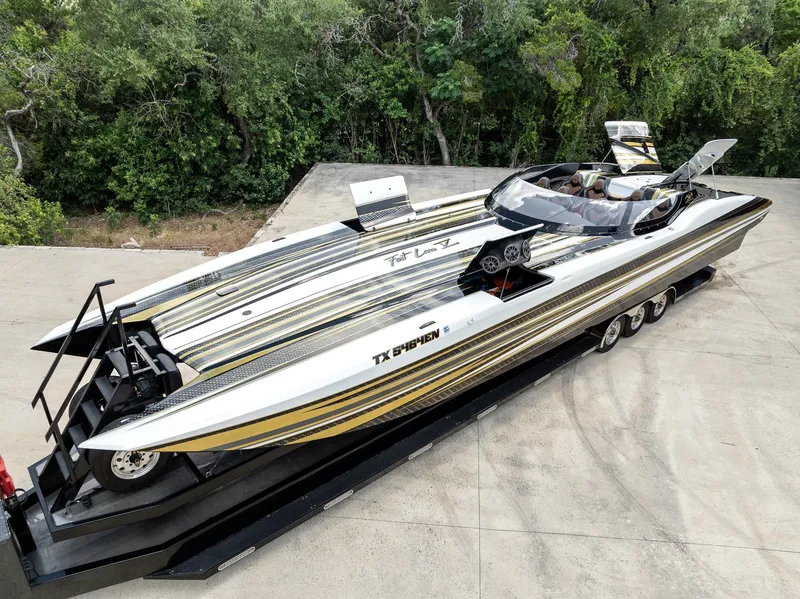Slide: The Image of 2017 MTI 48 speedboat on trailer, sleek design, parked outdoors with lush greenery background. - 17