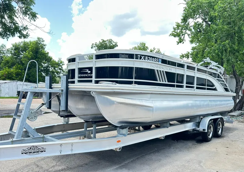 Slide: The Image of 2021 Bennington L 24 Swingback pontoon boat on trailer, parked outdoors. - 2