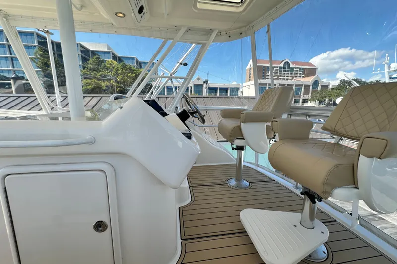 Slide: The Image of 2005 Riviera 47 Open Flybridge interior with helm and seating, docked near modern buildings. - 22