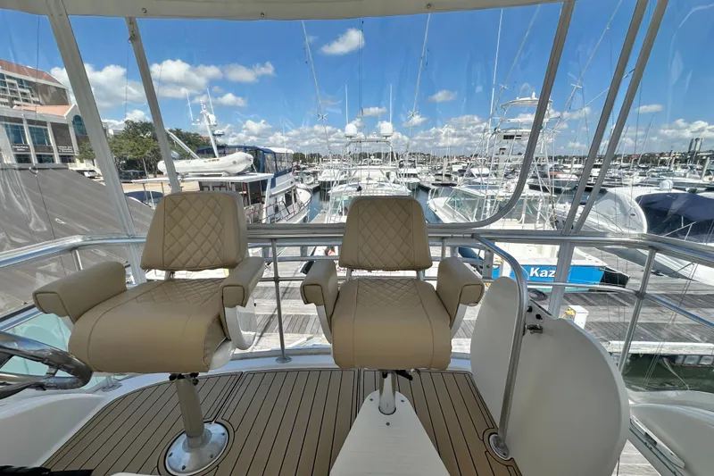 Slide: The Image of 2005 Riviera 47 Open Flybridge yacht interior with two beige captain chairs overlooking marina. - 30