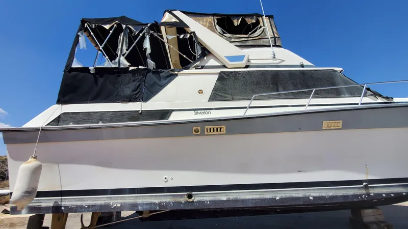 Slide: The Image of 1985 Silverton 40 Aft Cabin boat with damaged canopy, displayed on land under clear blue sky. - 35