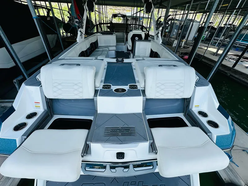 Slide: The Image of 2023 Malibu 25LSV boat interior with white seating and cup holders in a marina. - 12