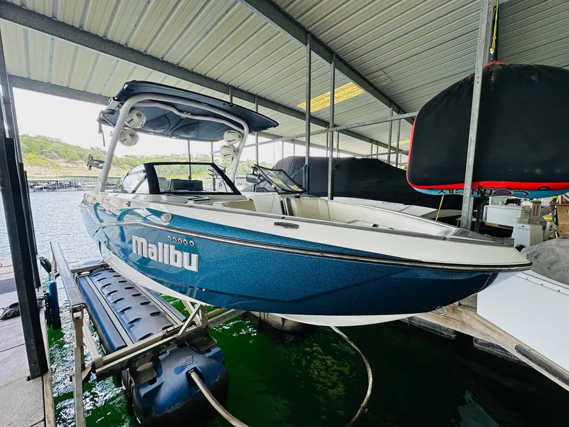 Slide: The Image of 2023 Malibu 25LSV boat in dock, blue exterior, under covered marina. - 7