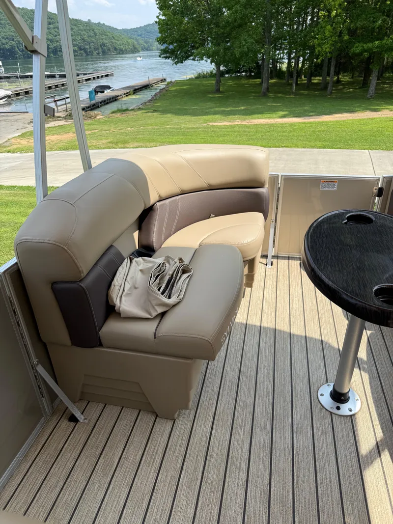 Slide: The Image of 2021 Sylvan Mirage 822 PARTY FISH boat interior with seating and table, near a scenic lake. - 6