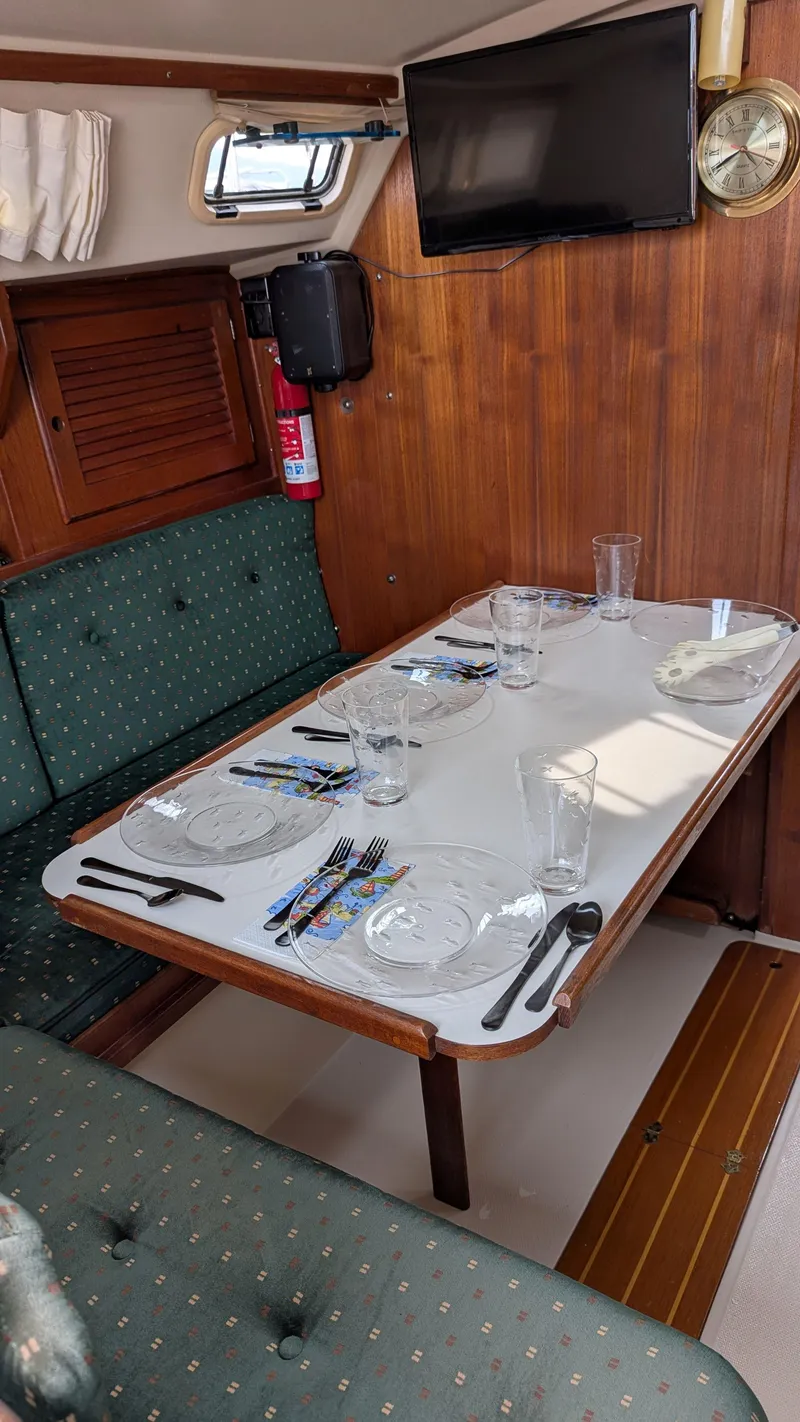 Slide: The Image of 1988 Catalina 30 MkII interior dining area with set table, green seating, and mounted TV. - 19