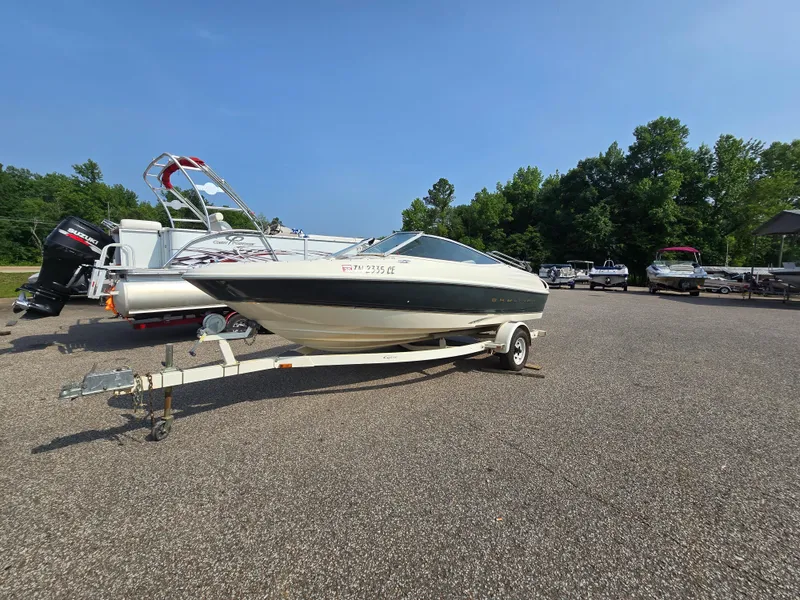 The Image of 1998 Bayliner 1850 Bs boat on trailer in parking lot, surrounded by trees and other boats. - 1