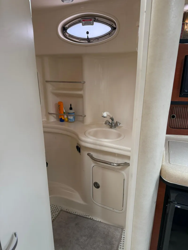 Slide: The Image of 2004 Sea Ray 300 Sundancer bathroom with sink, shelves, and porthole window. - 11