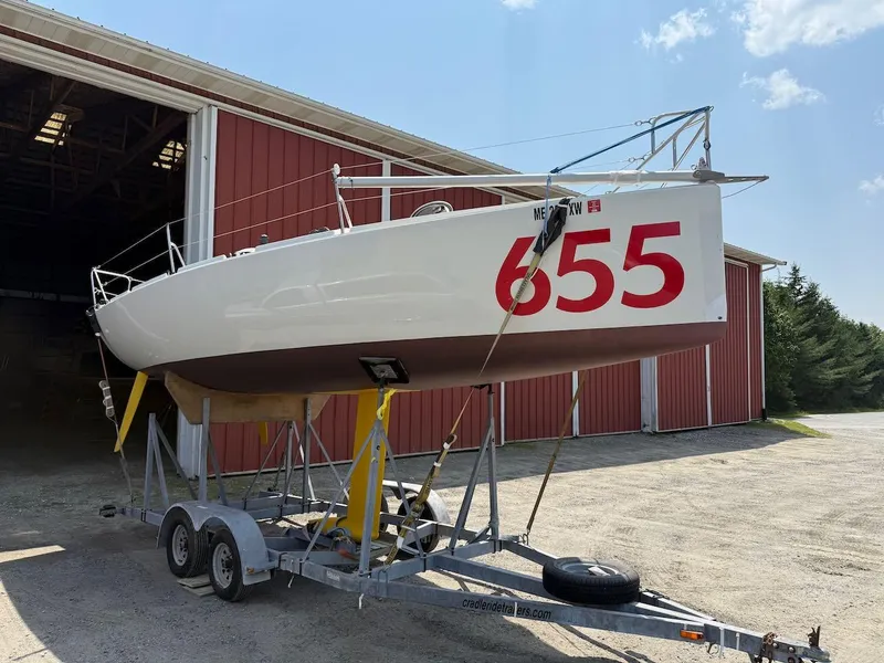 Slide: The Image of 2006 Mas Mini Transat 6.50 sailboat on trailer, red barn background. - 2