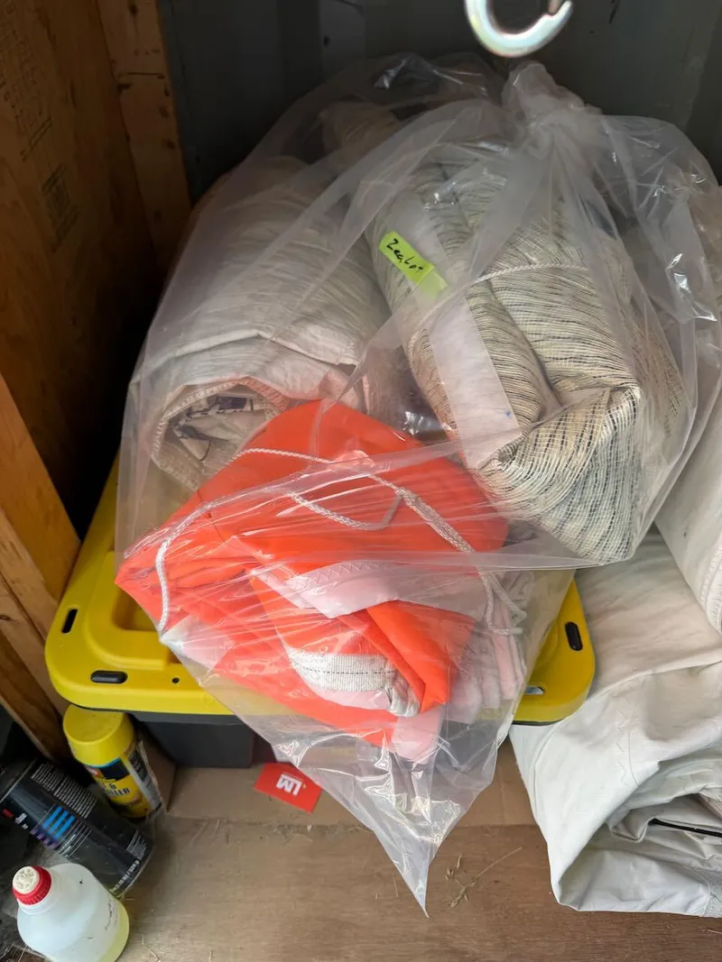 Slide: The Image of Stored sails in plastic bags for Mas Mini Transat 6.50, 2006 model, with visible orange fabric. - 25