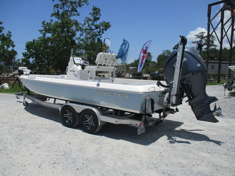 Slide: The Image of 2023 Skeeter SX 240 boat on trailer, parked outdoors with trees and flags in background. - 5