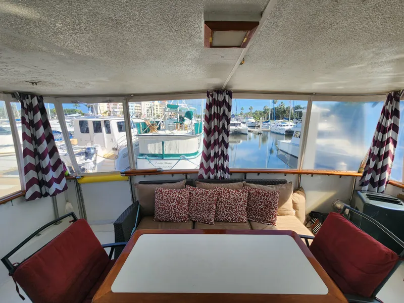 Slide: The Image of 1979 Hatteras 58 Long Range Cruiser interior with marina view, featuring cozy seating and patterned curtains. - 14