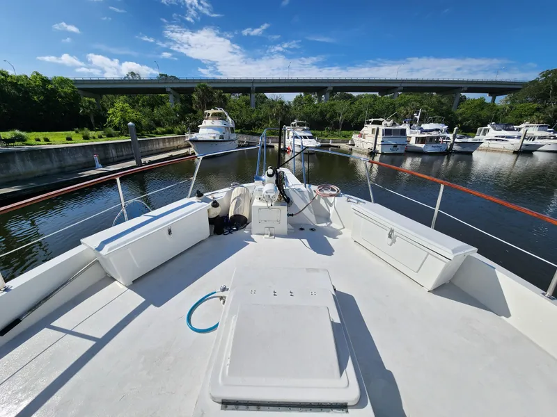 Slide: The Image of 1979 Hatteras 58 Long Range Cruiser docked in a scenic marina under a clear blue sky. - 22