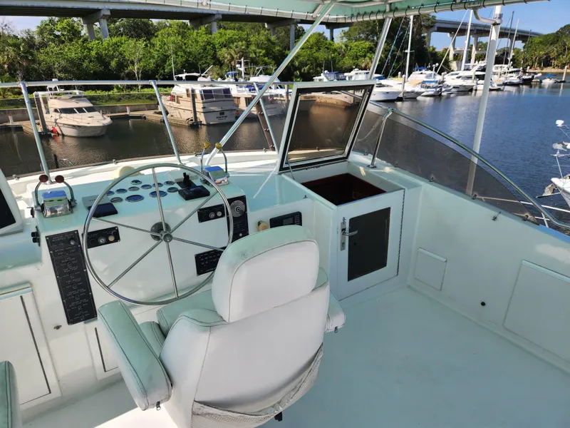 Slide: The Image of 1979 Hatteras 58 Long Range Cruiser helm with marina view, featuring classic controls and white seating. - 35