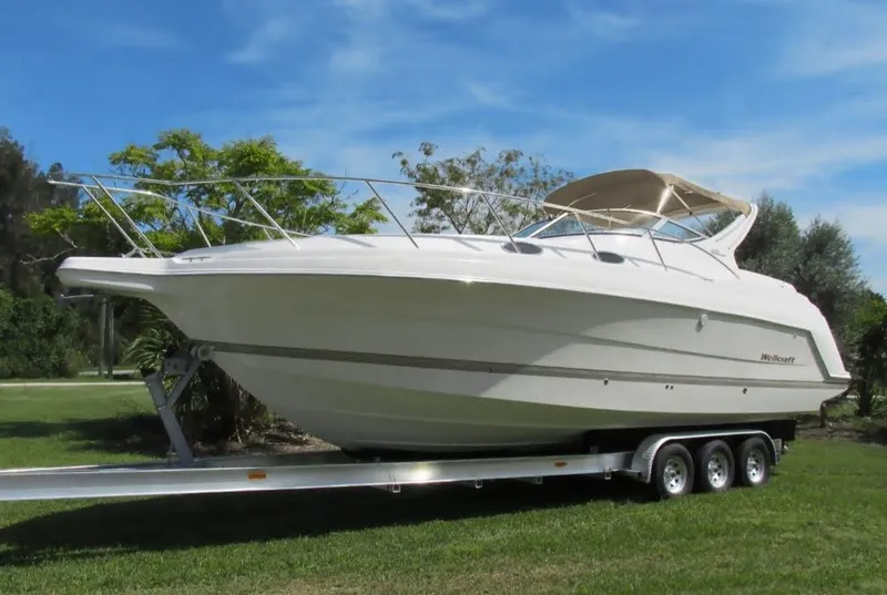 The Image of 2000 Wellcraft 3000 Martinique boat on a trailer, parked on grass under a clear blue sky. - 1