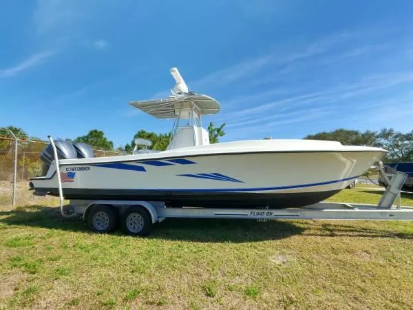 The Image of 1999 Contender 28 Sport boat on trailer, parked on grass under clear blue sky. - 0
