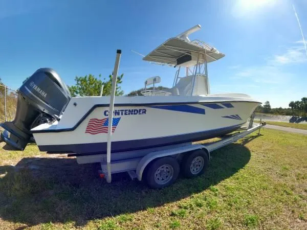 Slide: The Image of 1999 Contender 28 Sport boat on trailer with Yamaha engine, parked on grass under clear sky. - 2