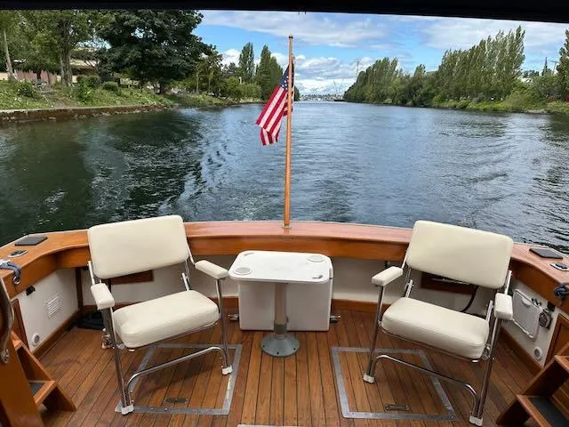 Slide: The Image of 1978 Egg Harbor 36 Sedan boat deck with chairs, table, and American flag on a scenic waterway. - 18