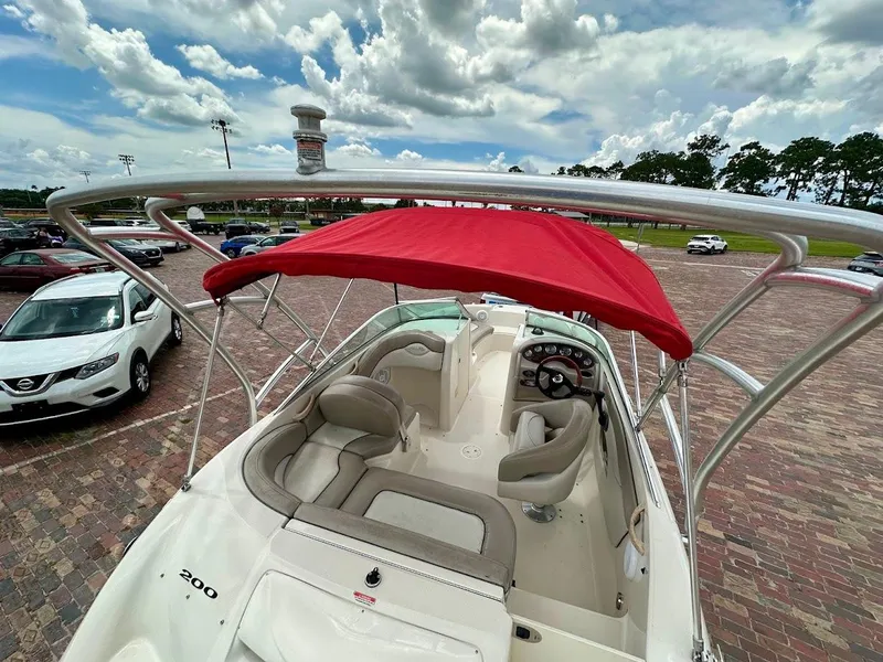 Slide: The Image of 2004 Sea Ray SunDeck 200 boat with red canopy, parked on brick pavement under cloudy sky. - 15