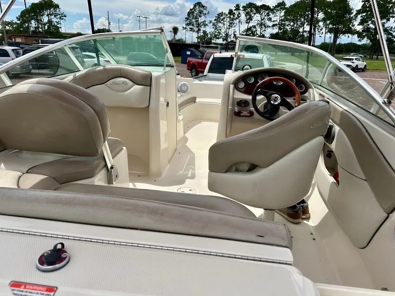 Slide: The Image of 2004 Sea Ray SunDeck 200 interior with beige seating and steering wheel, parked outdoors. - 16