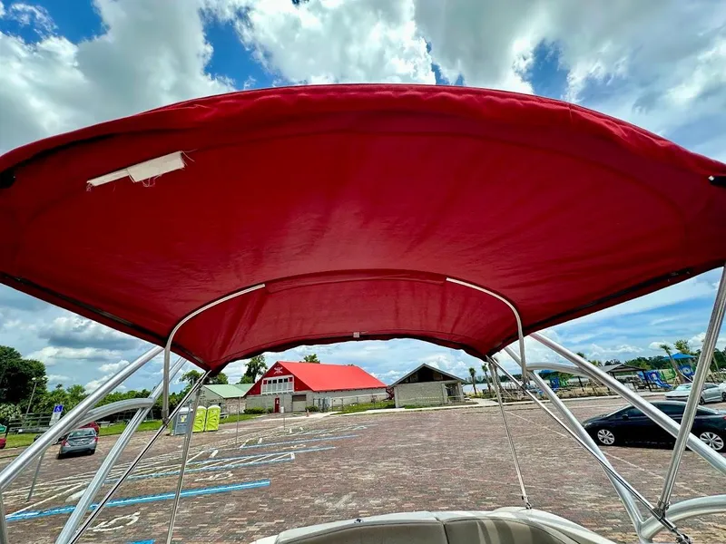 Slide: The Image of 2004 Sea Ray SunDeck 200 with red canopy, parked under a partly cloudy sky. - 17