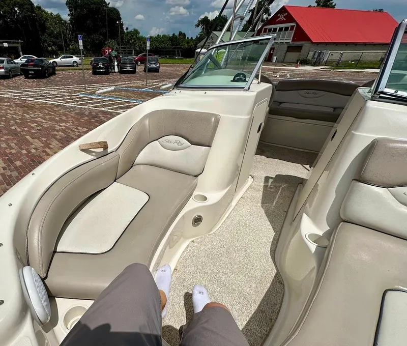 Slide: The Image of 2004 Sea Ray SunDeck 200 interior with beige seating, parked near a red-roofed building. - 35