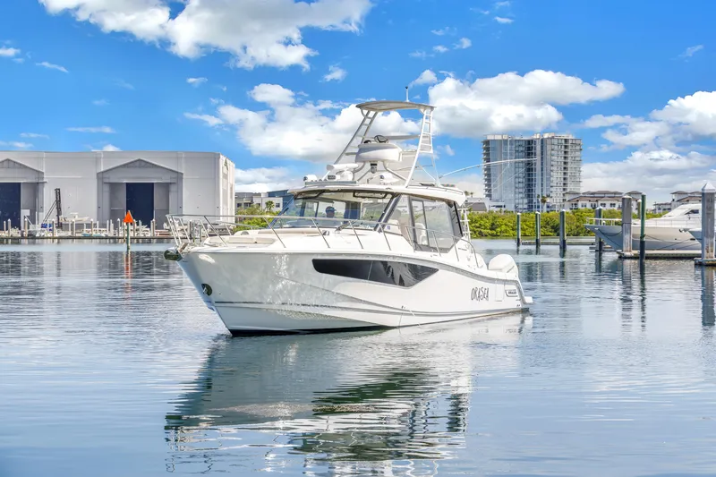 Slide: The Image of 2023 Boston Whaler 405 Conquest boat on calm water, with marina and buildings in background. - 14