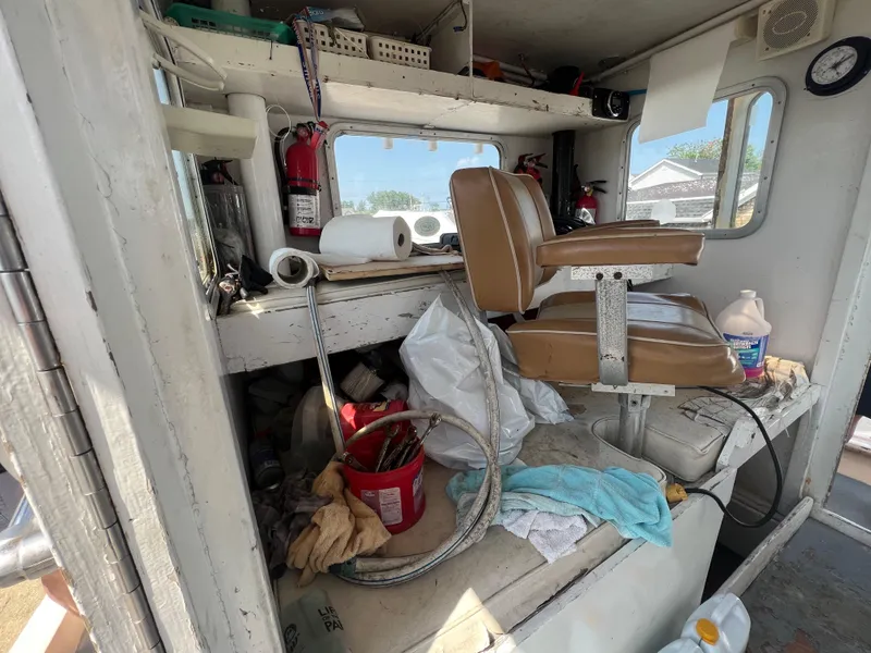Slide: The Image of Interior of a 1984 JC 35 boat with brown seat, cluttered shelves, and cleaning supplies. - 10
