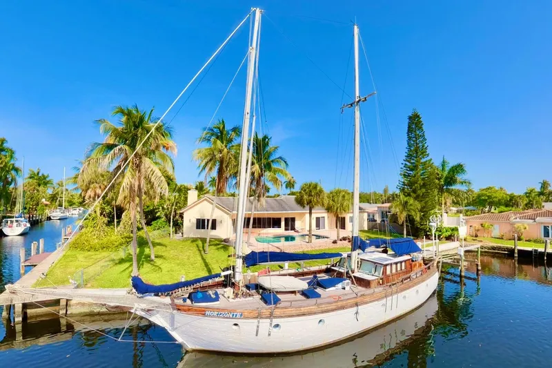 Slide: The Image of Schooner docked by waterfront home, surrounded by palm trees, under clear blue sky. - 1