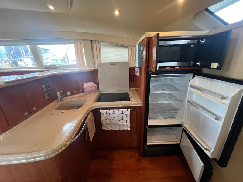 Slide: The Image of 2004 Sea Ray 480 Motor Yacht kitchen with open fridge, sink, and wooden cabinetry. - 35