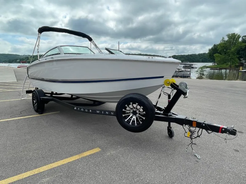 Slide: The Image of 2025 Four Winns H1 boat on trailer by a lake under cloudy sky. - 2