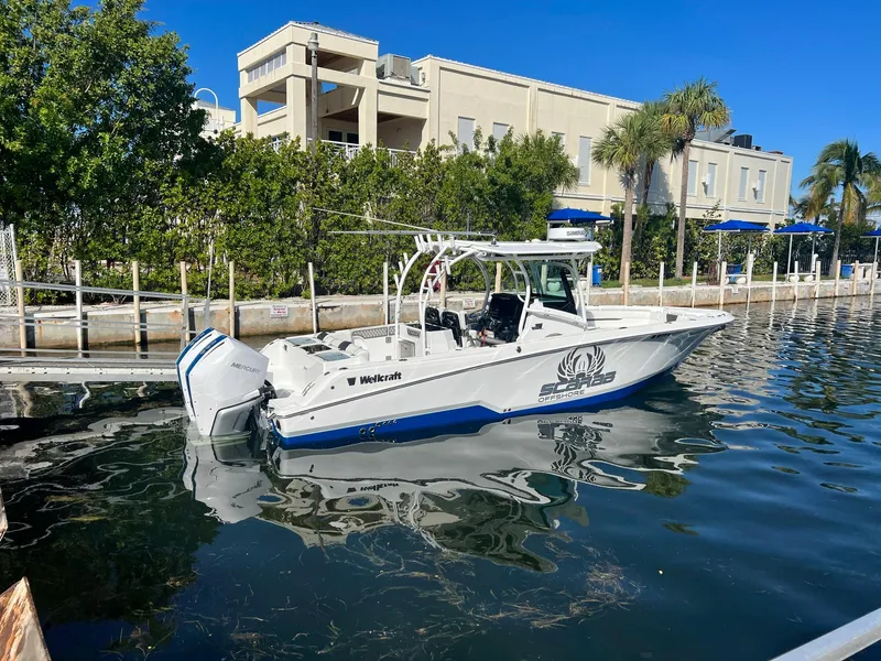 Slide: The Image of 2023 Wellcraft 302 Fisherman boat illuminated at night with blue lights, docked at a marina. - 2