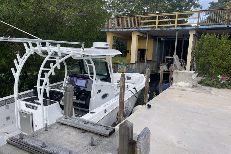Slide: The Image of 2023 Wellcraft 302 Fisherman boat docked near a wooden structure and lush greenery. - 29