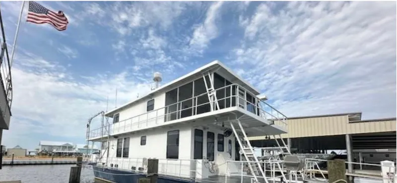 Slide: The Image of Custom 2003 houseboat docked under a cloudy sky with an American flag waving. - 3