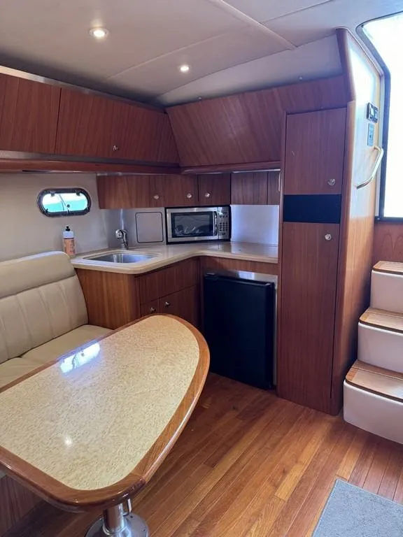 Slide: The Image of 2004 Tiara Yachts 3600 Sovran interior with kitchenette, dining area, and wooden cabinetry. - 13