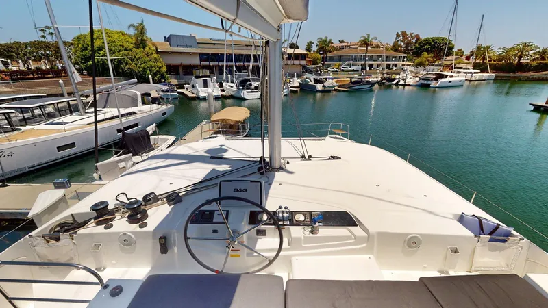 Slide: The Image of 2020 Lagoon 46 catamaran docked in a marina, featuring a spacious helm and serene water view. - 26