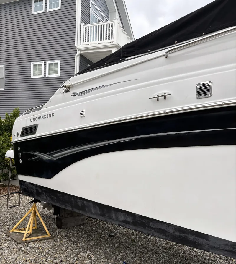 Slide: The Image of 2003 Crownline 262 CR boat on stands, near a gray house. - 12
