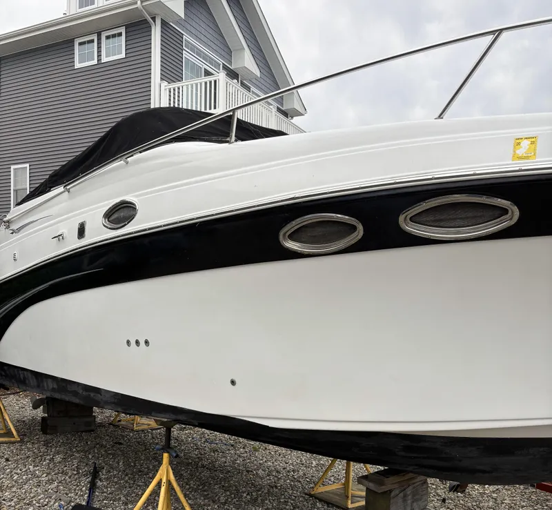 Slide: The Image of 2003 Crownline 262 CR boat on stands, near a modern house, overcast sky. - 13