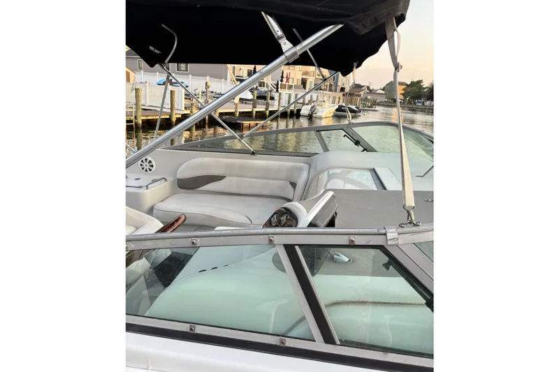 Slide: The Image of 2003 Crownline 262 CR boat interior with seating and canopy, docked by waterfront homes. - 17