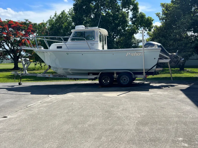 Slide: The Image of 2021 Parker 2120 boat on trailer, parked outdoors with trees in the background. - 11