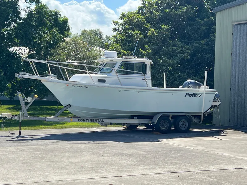 Slide: The Image of 2021 Parker 2120 boat on trailer, parked outdoors near trees and a building. - 2