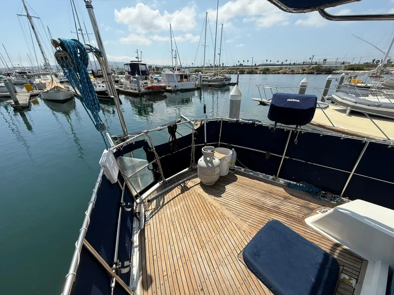 Slide: The Image of Deck of 1985 Nauticat 43 sailboat in marina, featuring wooden flooring and moored boats. - 6