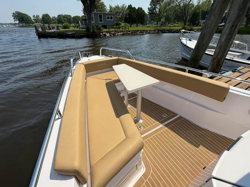 Slide: The Image of 2021 Axopar 28 CABIN boat with tan seating and table, docked by a scenic shoreline. - 20