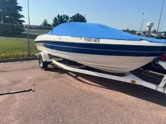 The Image of 2005 Bayliner 205 Bowrider boat on trailer with blue cover, parked outdoors. - 0