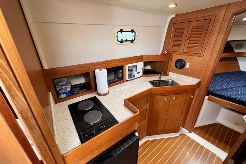 Slide: The Image of 2001 Mainship 34 PILOT yacht interior with kitchenette, featuring stove, sink, and wooden cabinetry. - 27
