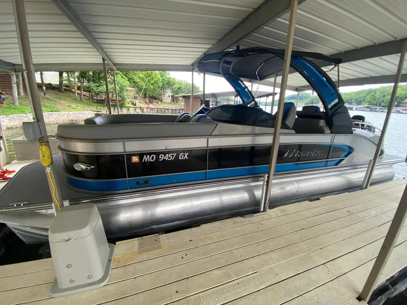 Slide: The Image of 2022 Manitou 25 LX SRW SHP pontoon boat docked under a covered marina. - 11