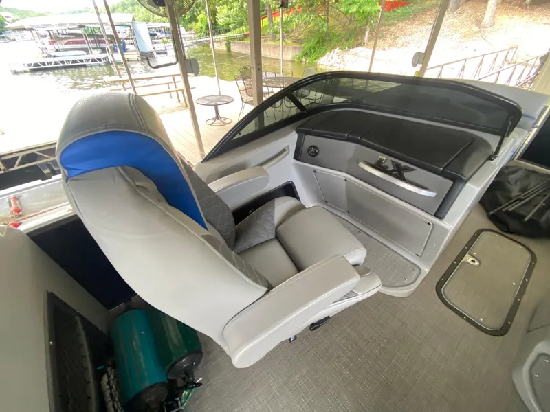 Slide: The Image of 2022 Manitou 25 LX SRW SHP boat interior with gray seating and helm, dockside view. - 21